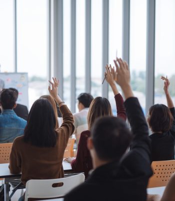 Raised up hands and arms of large group in seminar class room to agree with speaker at conference seminar meeting room